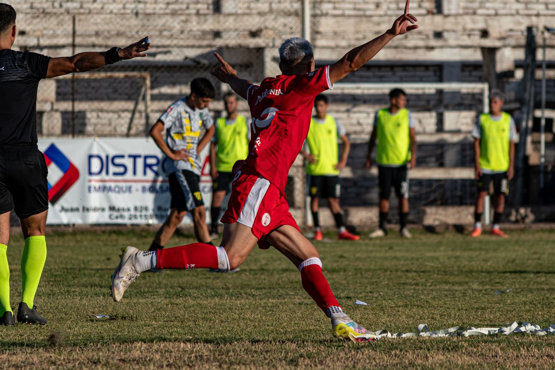 A soccer player in red celebrates a goal with enthusiasm on an outdoor field.
