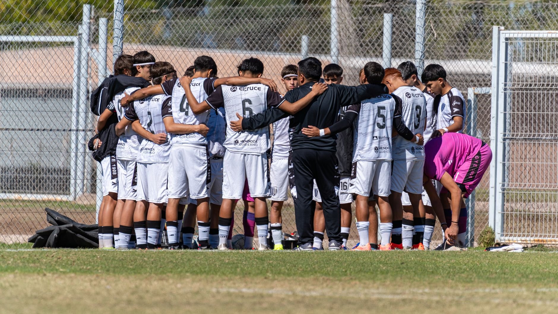 A youth soccer team huddles for motivation before a match on a sunny day.