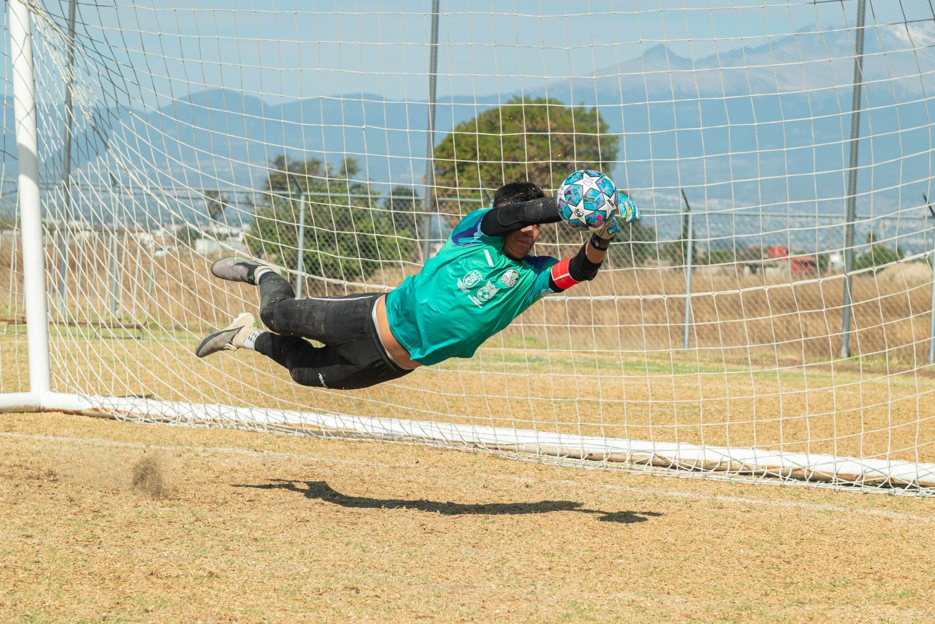 Dynamic action shot of a soccer goalkeeper making a diving save during a match in Puebla, México.