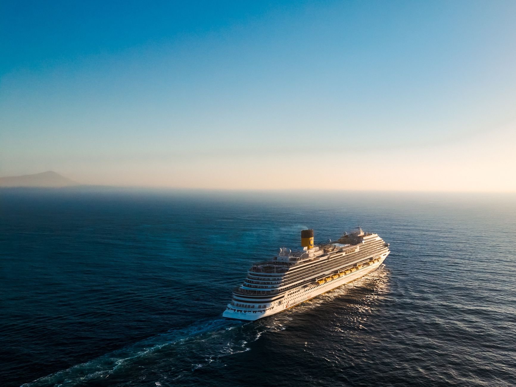 Aerial view of a luxury cruise ship navigating the calm ocean at sunset