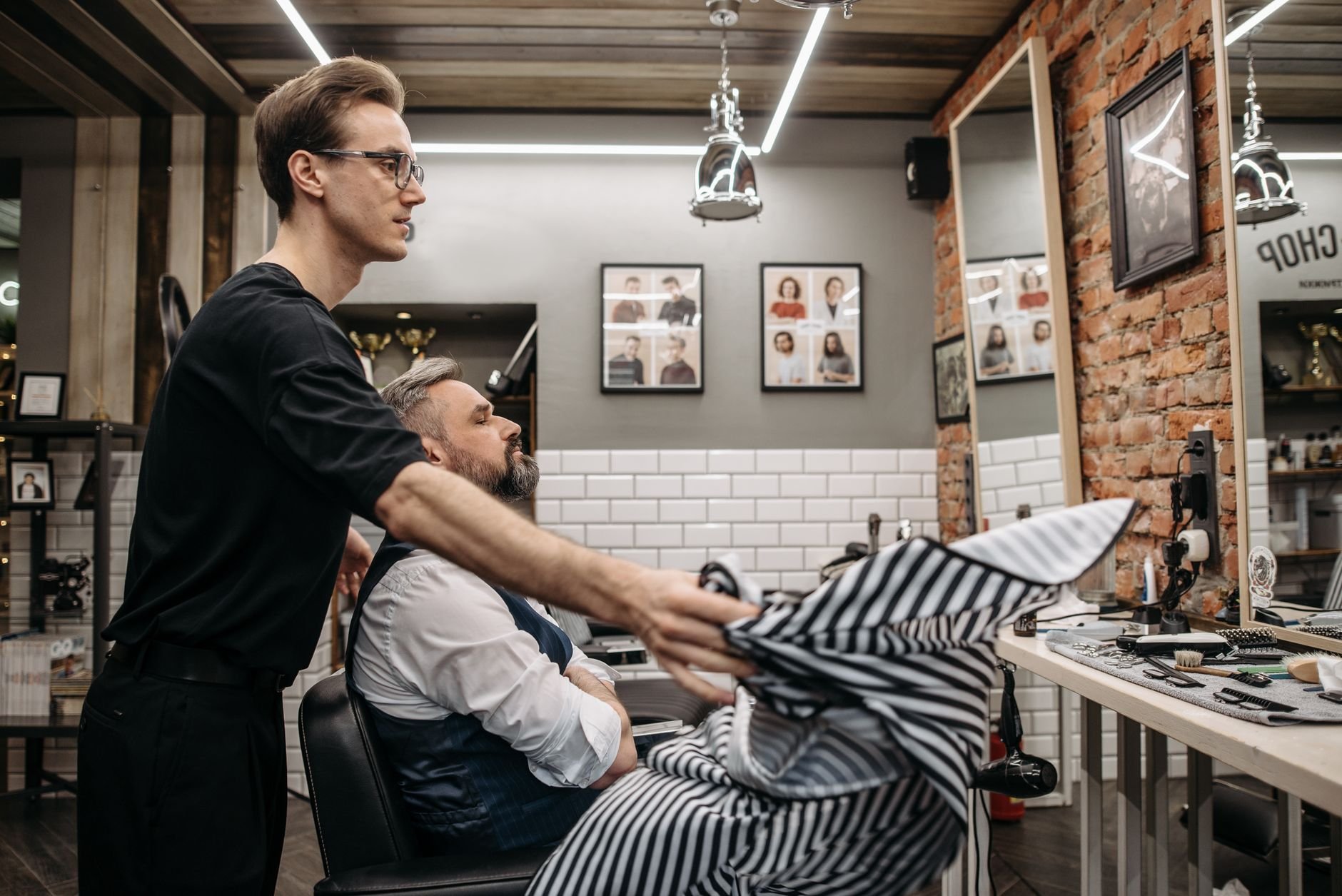 A barber prepares a client in a trendy barbershop with contemporary decor and styling tools.