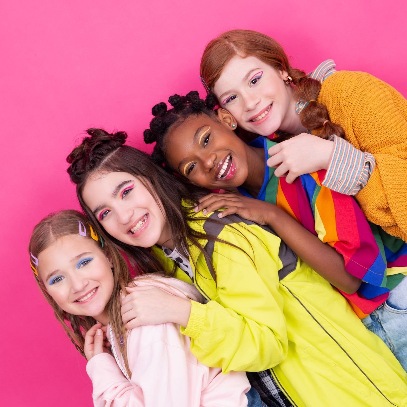 Colorful group portrait of teenage girls posing joyfully against a pink background.
