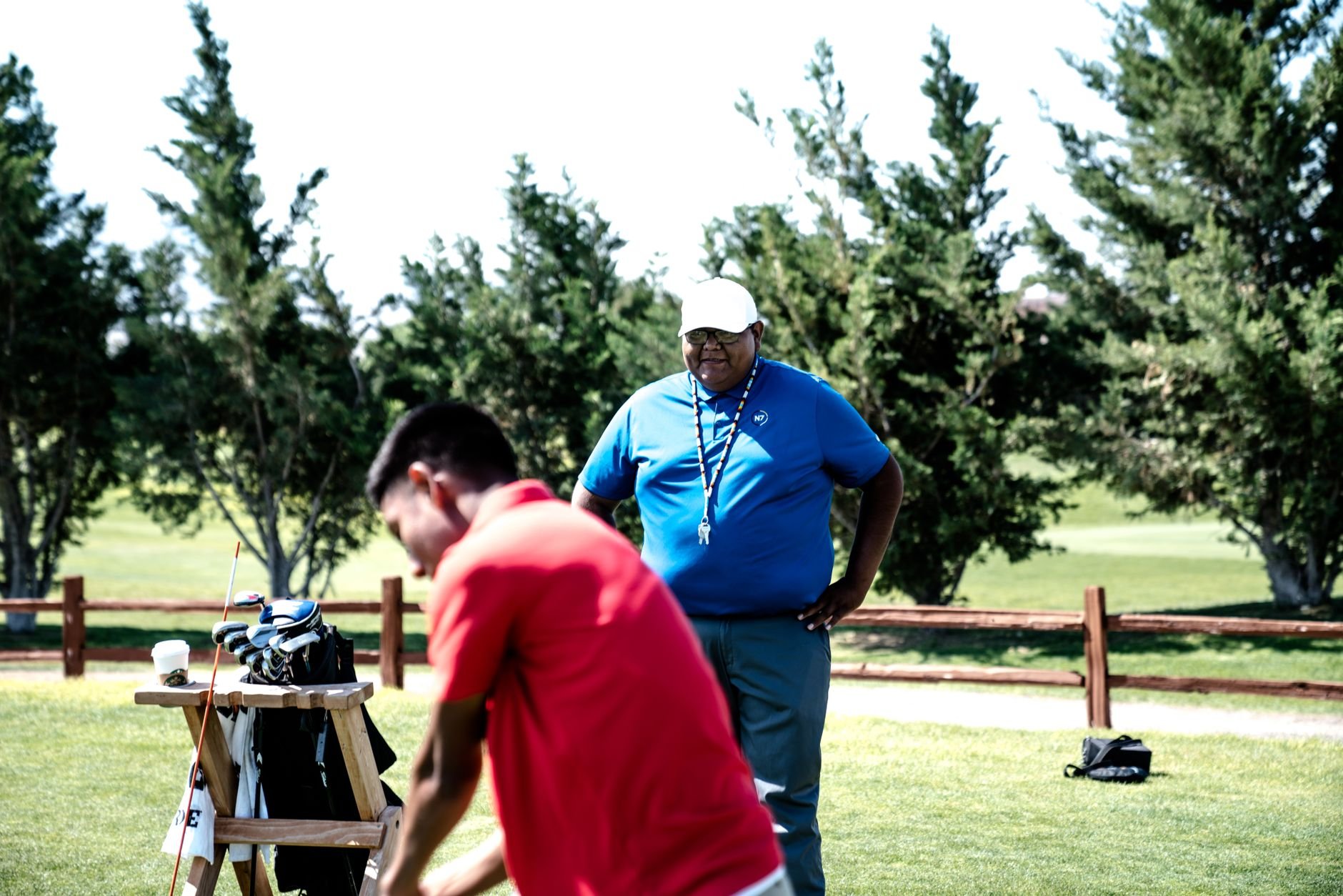 Two golfers on a sunny golf course, one practicing and a caddie observing.