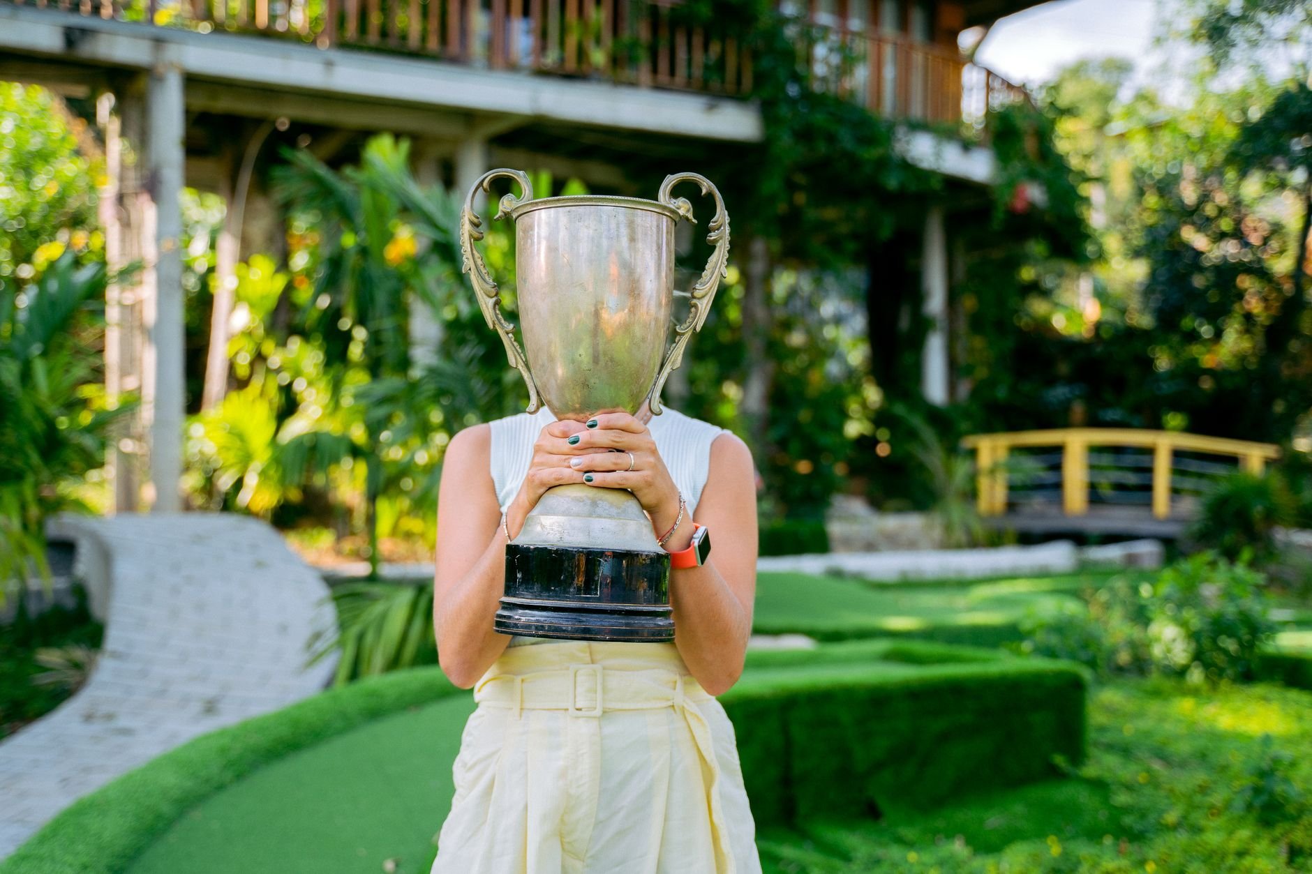 Female golfer holding a large trophy in a lush outdoor setting, celebrating her victory.