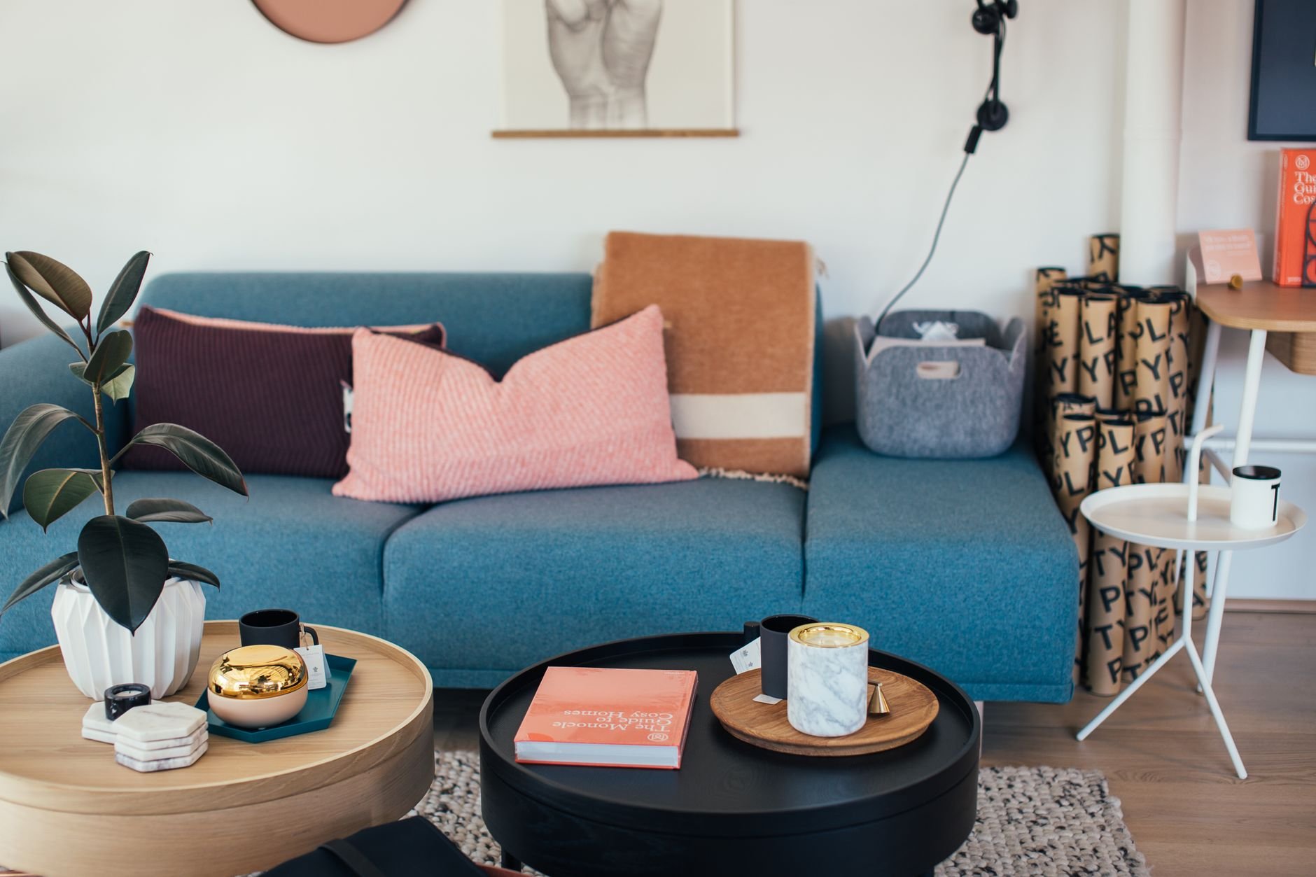 Comfortable sofa with cushions placed in cozy living room near small round coffee tables decorated with potted plant and candles