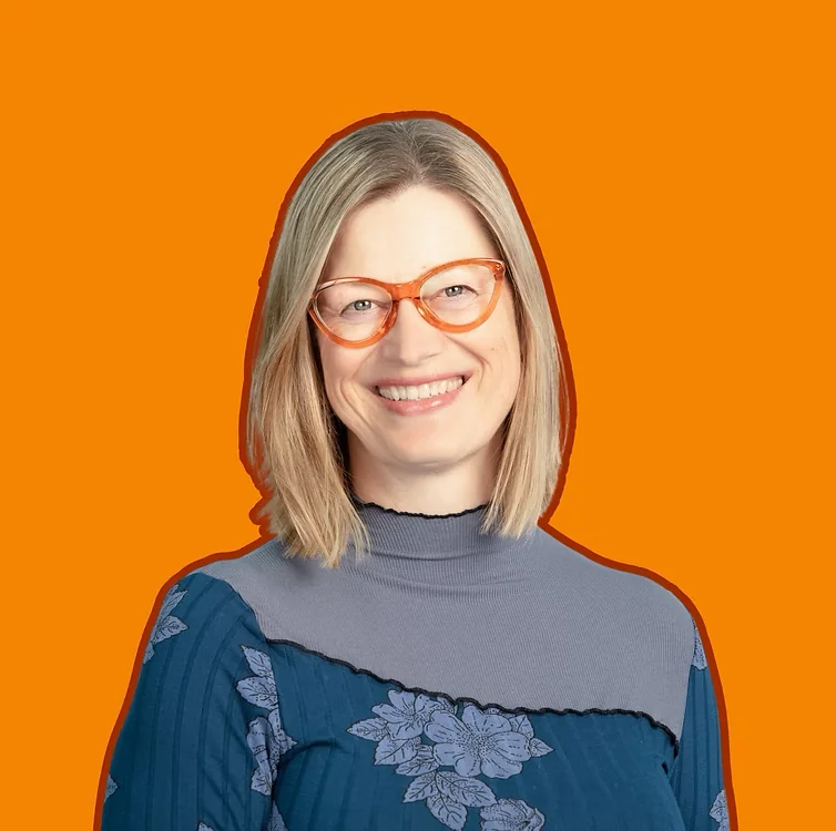 Dorien Morin-van Dam smiling, wearing orange glasses and a blue floral top against an orange background