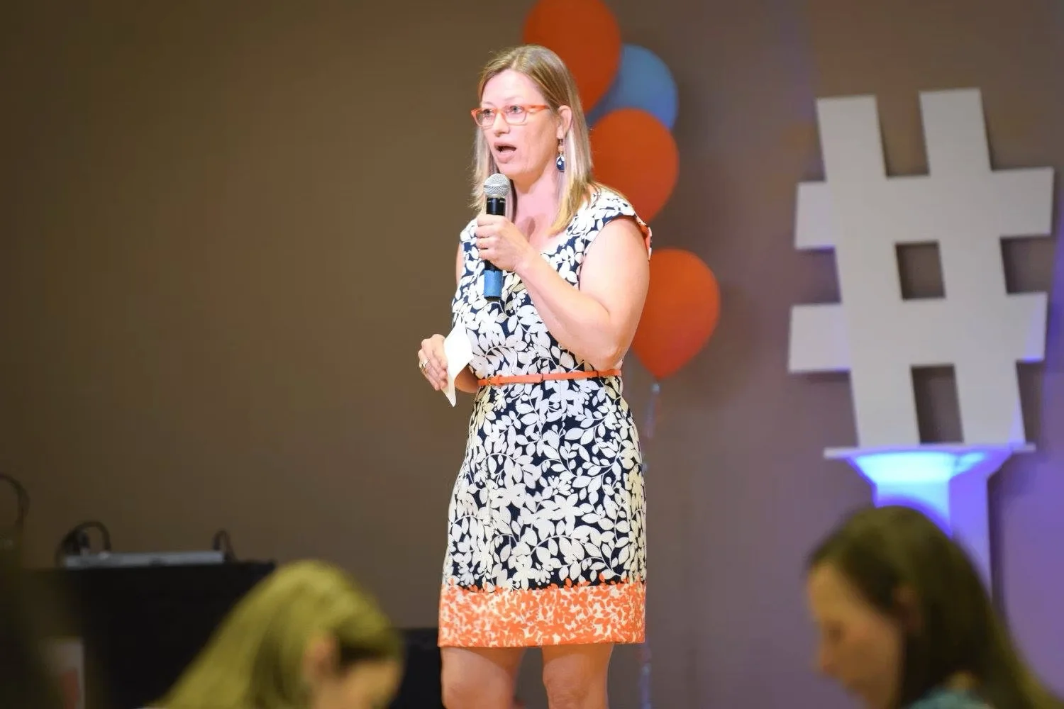 Dorien Morin-van Dam speaking on stage with a microphone, hashtag sign in background