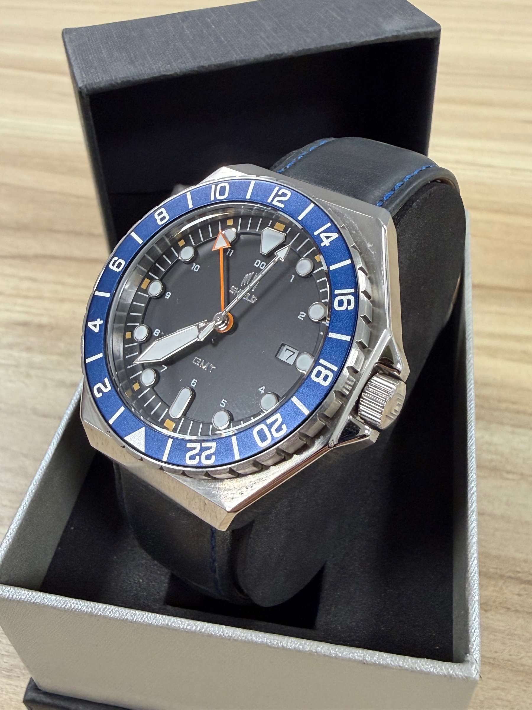 Shield Marco GMT closeup showing blue bezel, black dial, orange GMT hand and date window