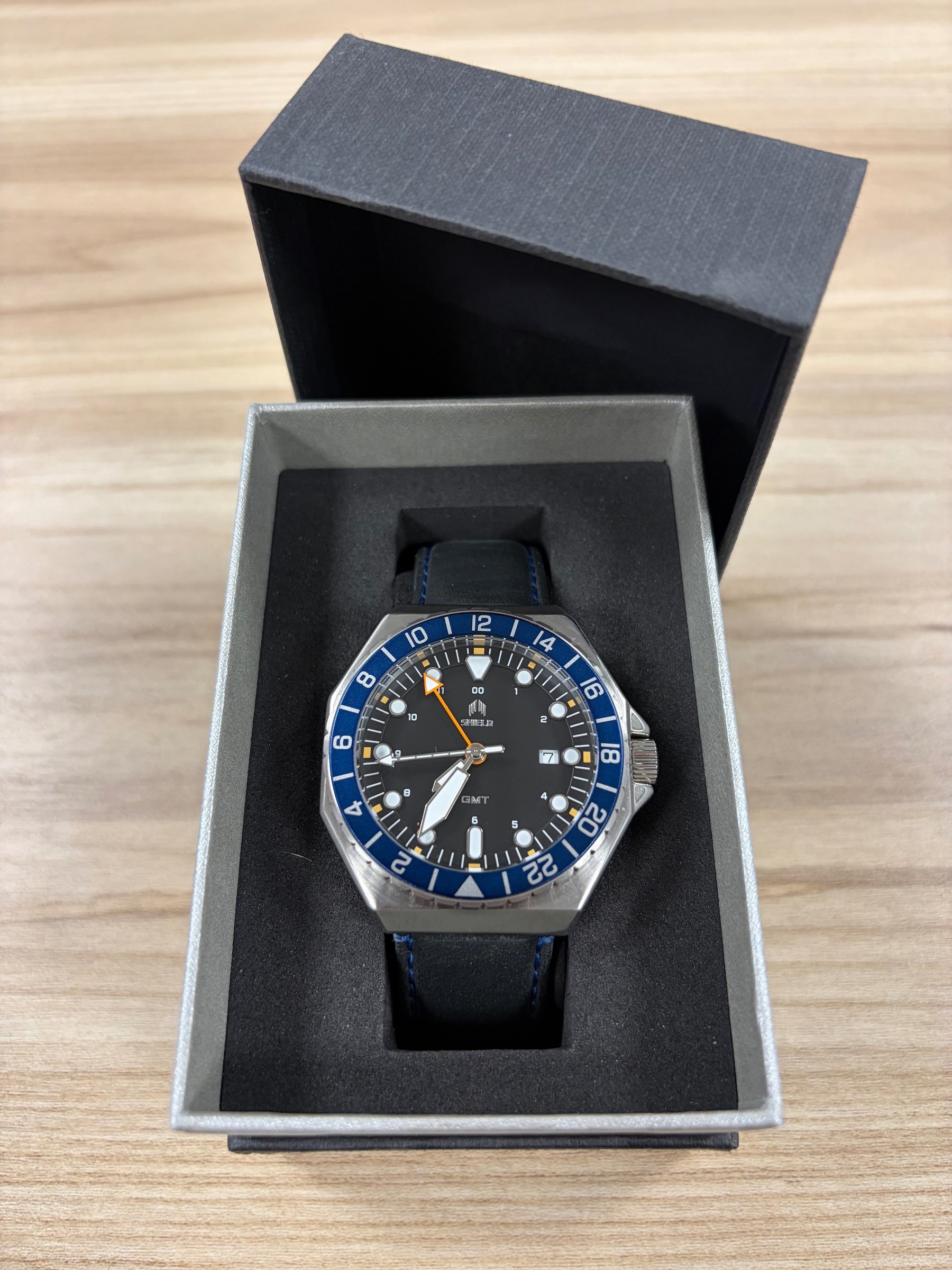 Shield Marco GMT watch in open black box, blue bezel with orange GMT hand, black dial, blue leather strap