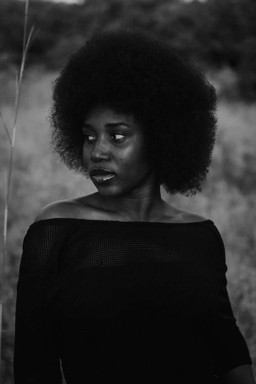 Artistic portrait of a woman with afro hair in a natural setting.