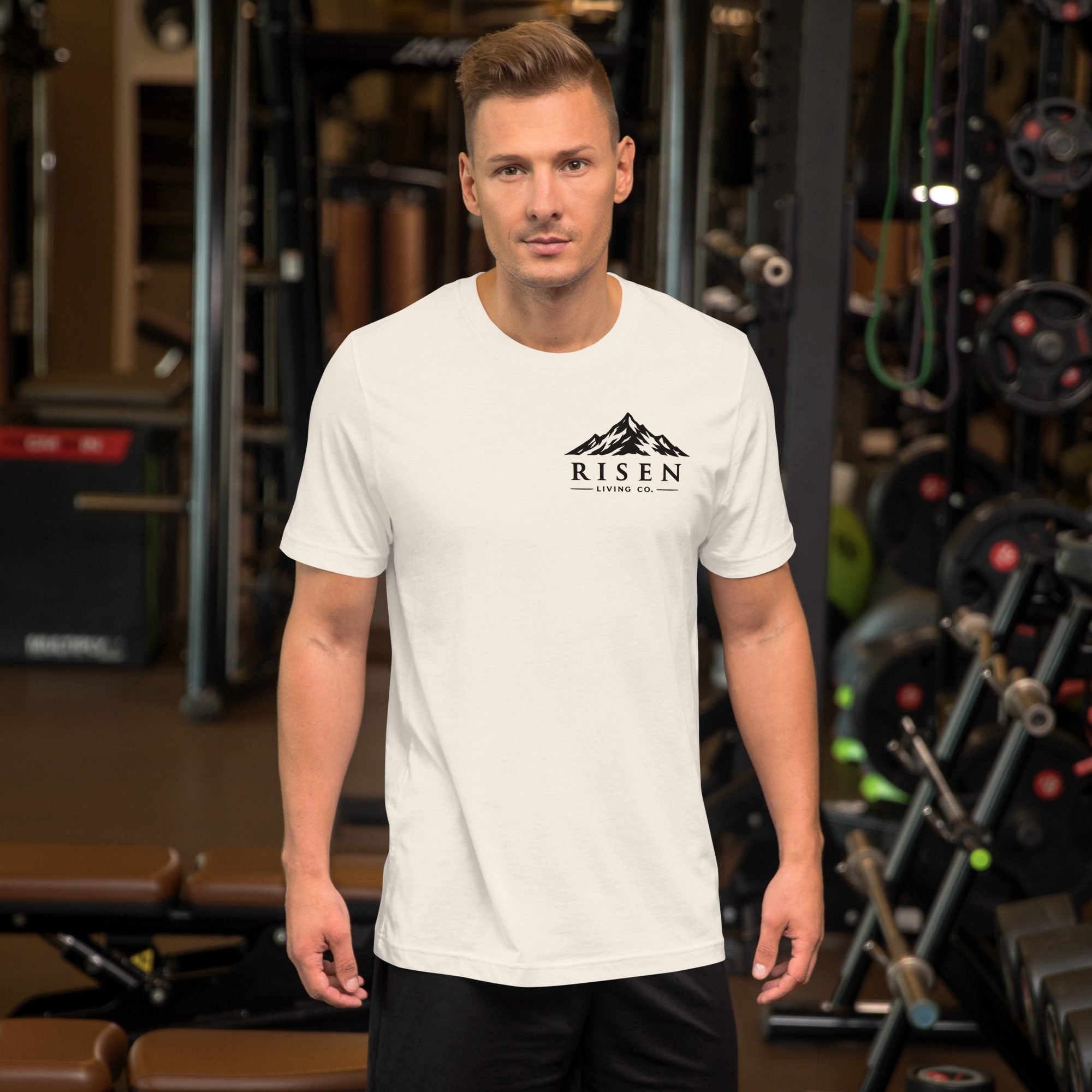 Man wearing Risen Living Co. mountain wordmark tee in vintage white, gym setting