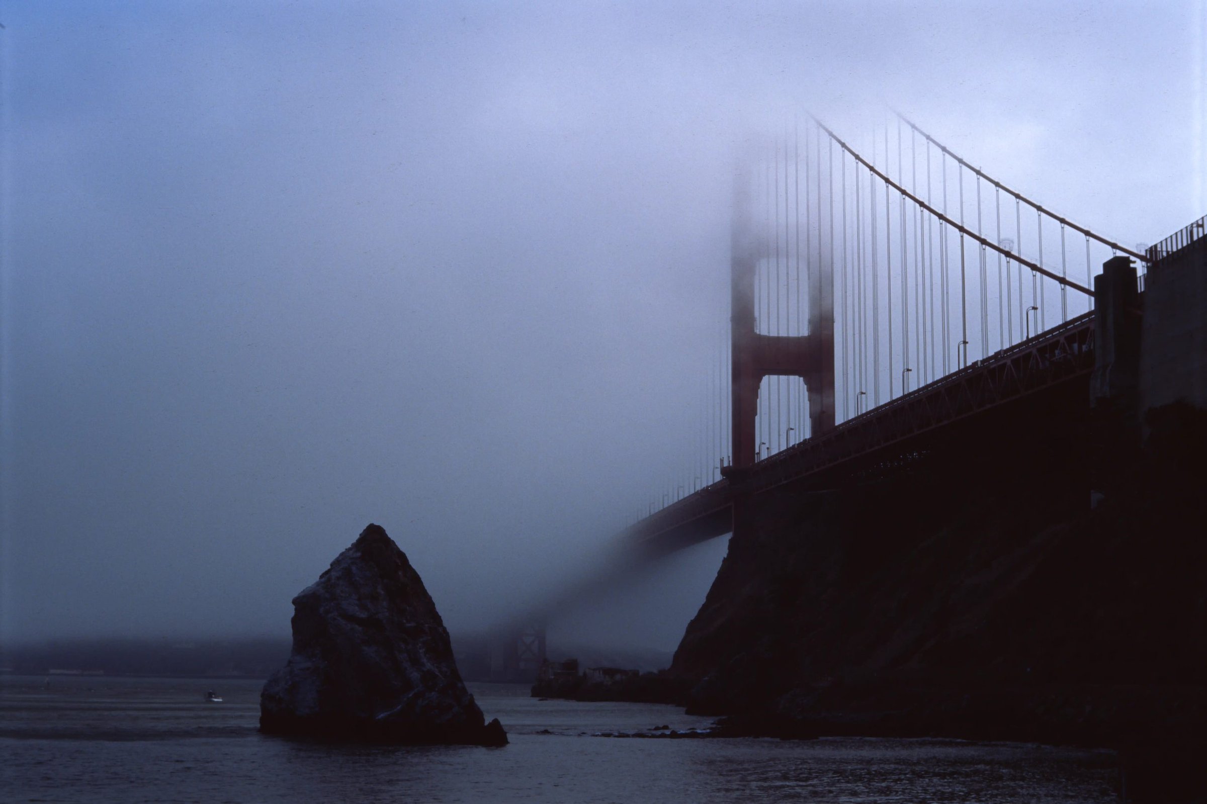 Golden Gate Bridge emerging from thick fog, dark and dramatic, film photograph