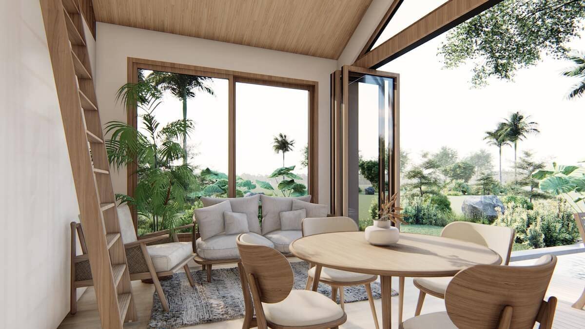 Tiny home interior with vaulted wood ceiling, lounge seating, dining table, and floor-to-ceiling windows overlooking tropical garden