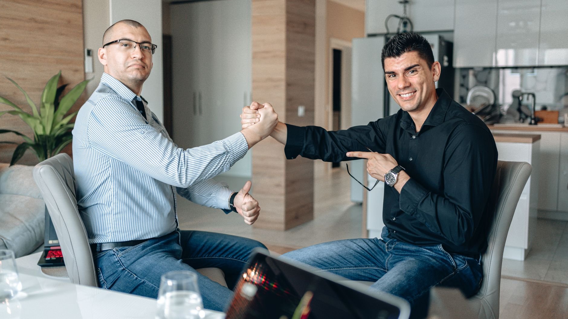 Two businessmen in casual attire shaking hands and smiling at an office meeting.