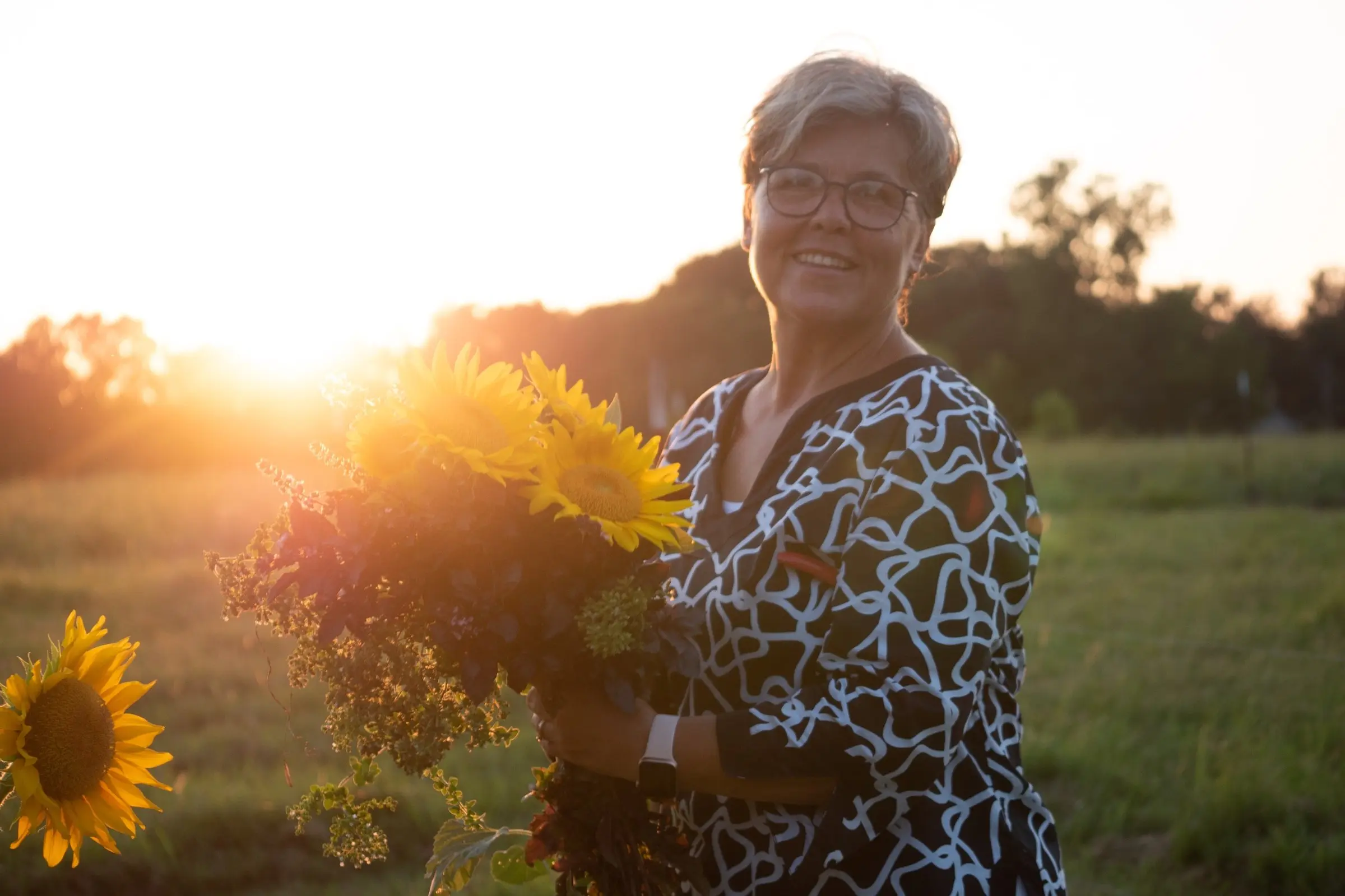 Mechel, founder of Riverbend Hollow, holding sunflowers in a golden sunset field