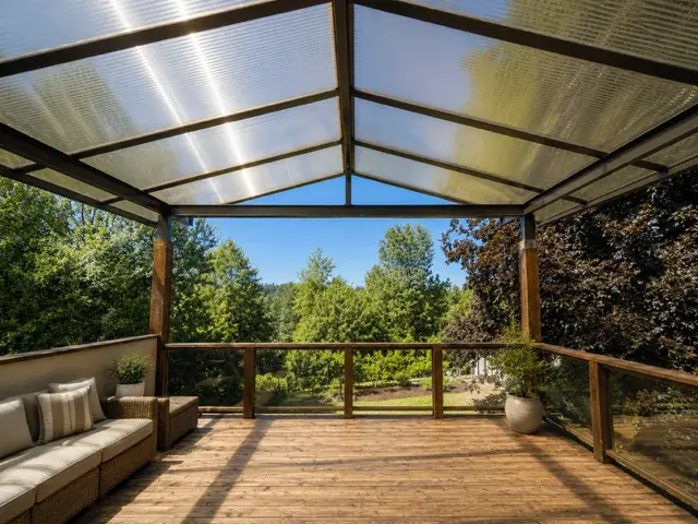 Open air covered deck with polycarbonate gable roof overlooking lush backyard